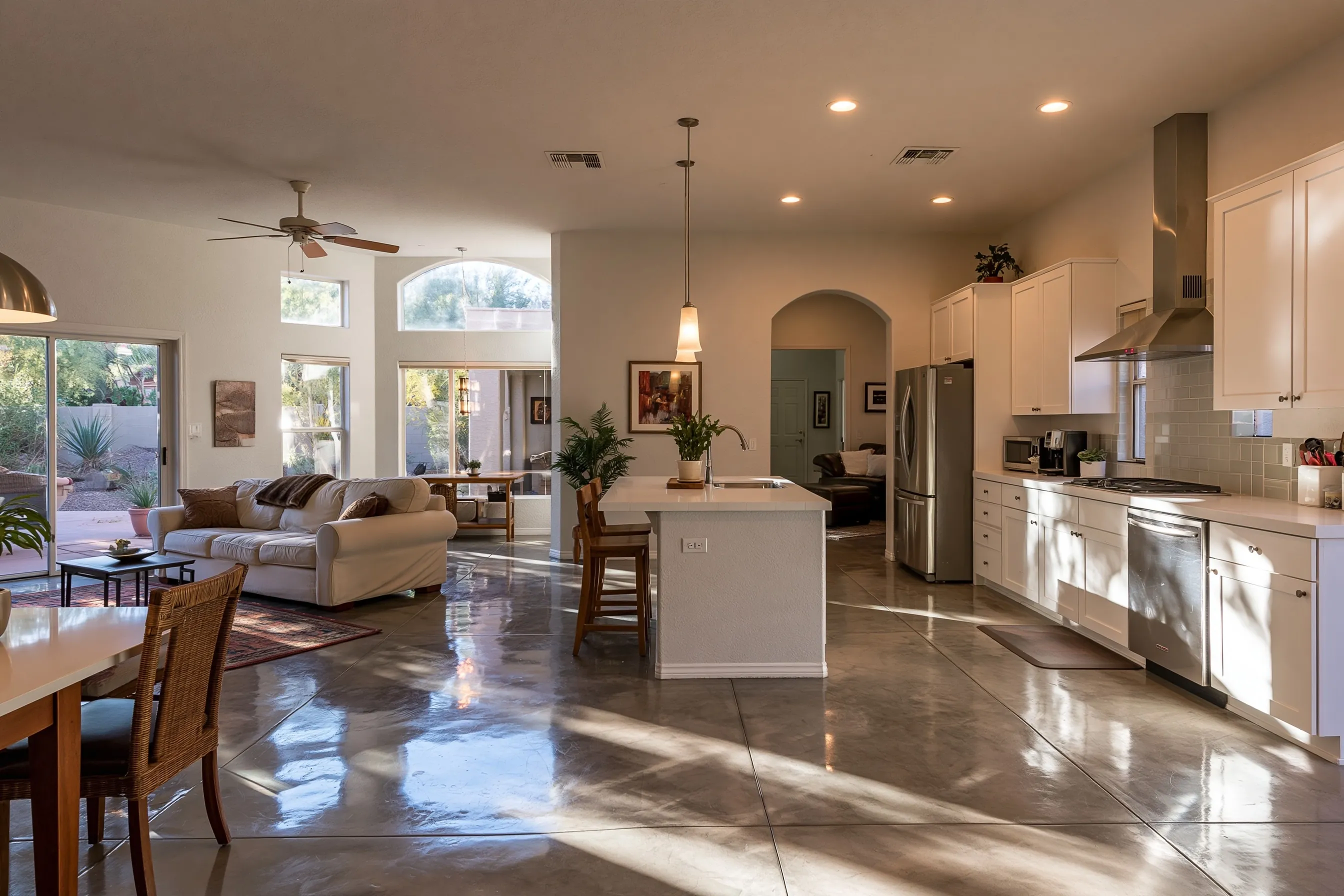 Kitchen and great room with a warm grey polished concrete floor, light reflecting from a window, white cabinets and stucco walls